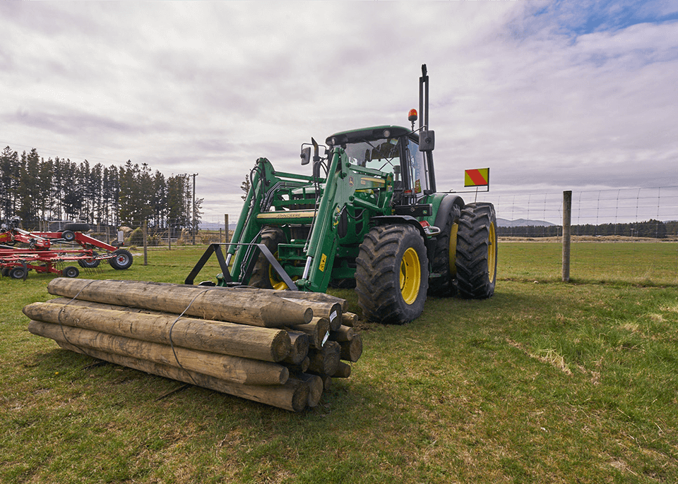 Green tractor picking up fence posts.